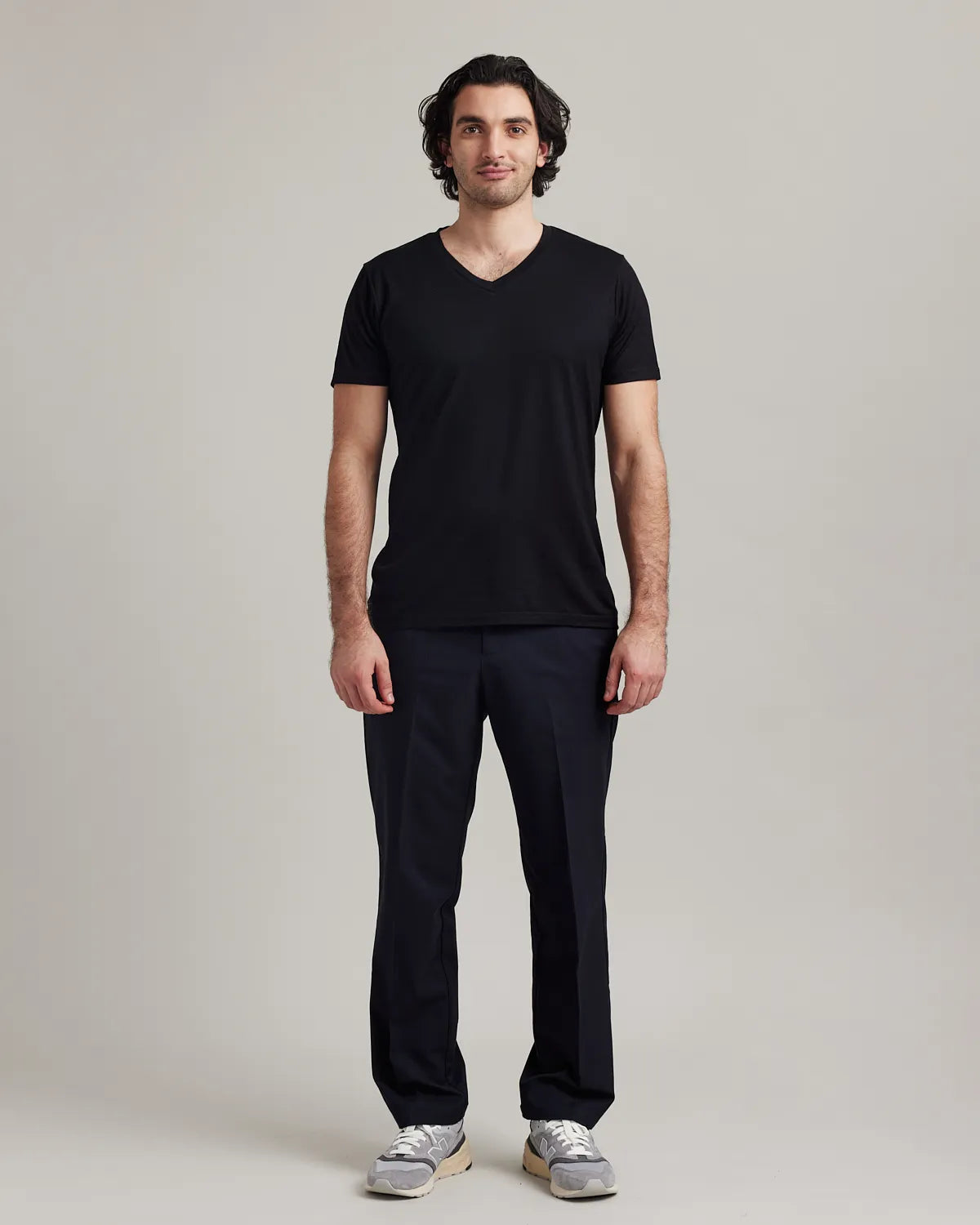 Man wearing a black merino V-neck t-shirt and dark pants on a plain background