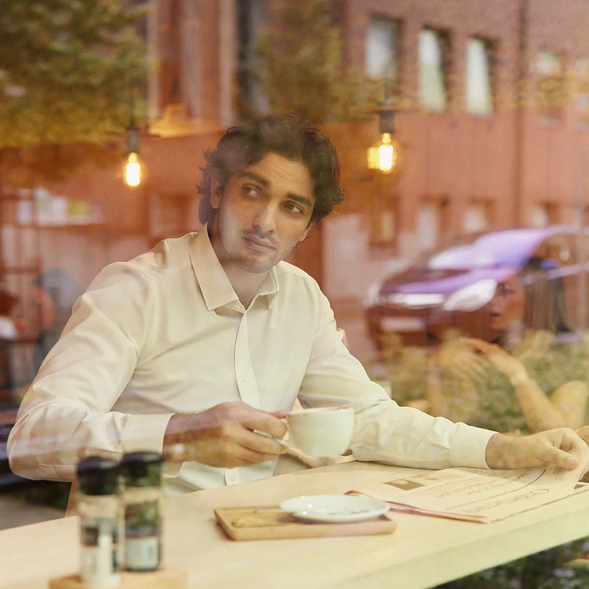 Man holding a coffee in a coffee bar wearing a white merinowool dress shirt from Wolk