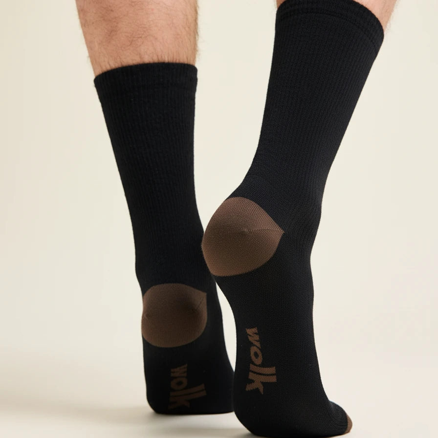 Black merino wool socks with brown accents and Wolk logo worn by a person on a beige background