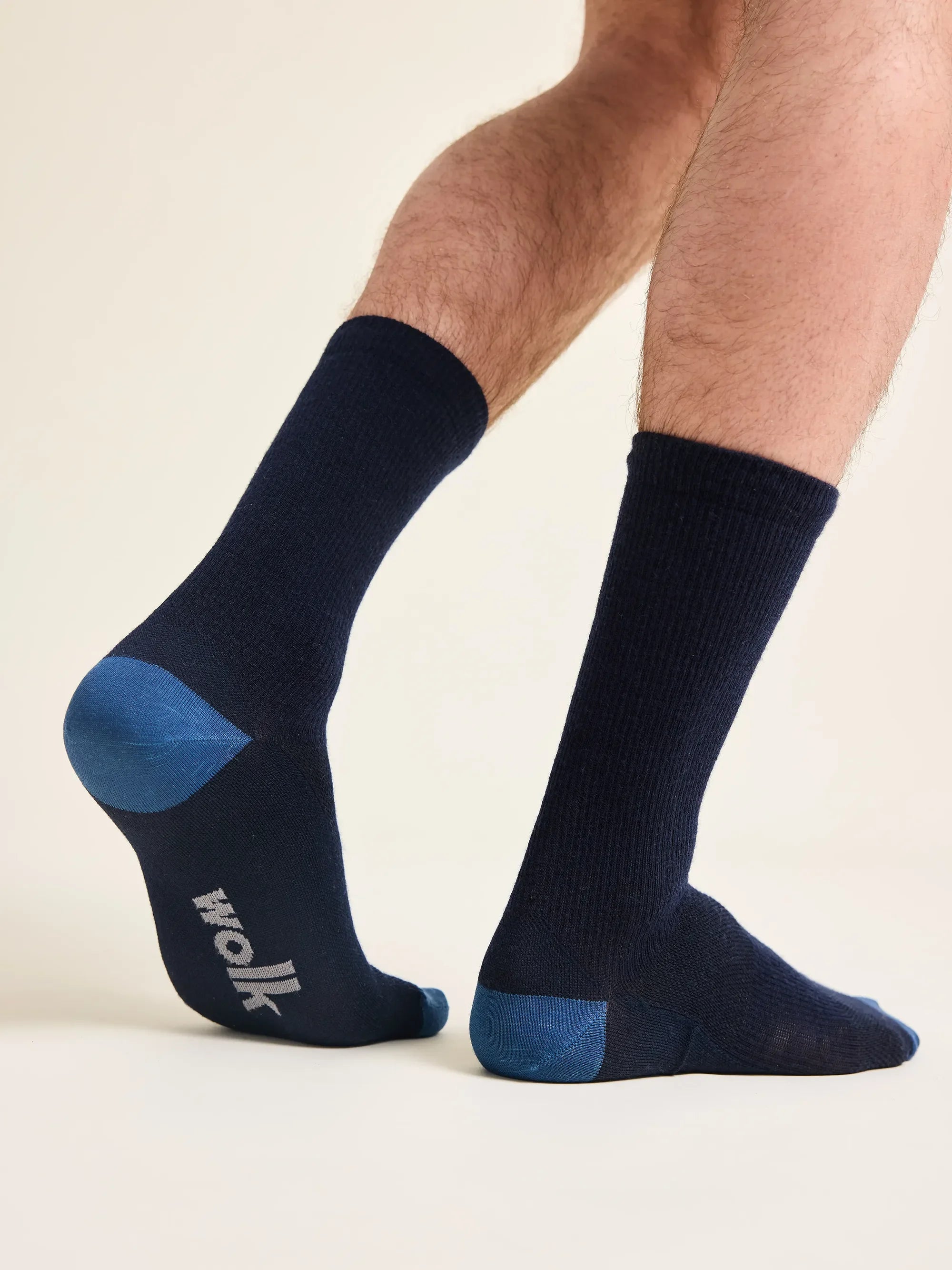 Man wears mid high merino wool socks in navy color with blue heel and light grey wolk logo on the foot bed