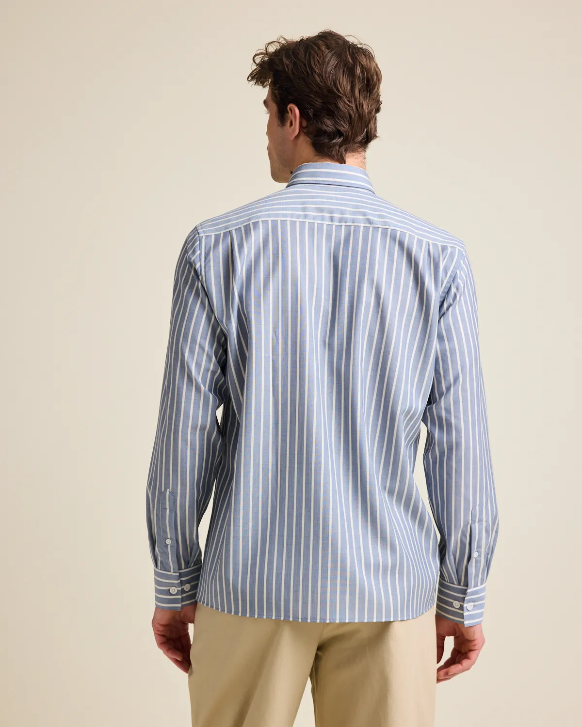 Back view of a man wearing a navy blue and white striped merino wool button up shirt against a beige background