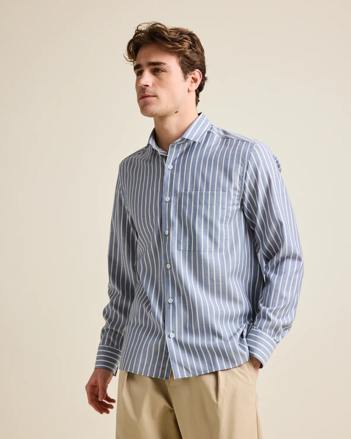 Man wearing a navy blue and white striped merino wool button up shirt against a beige background