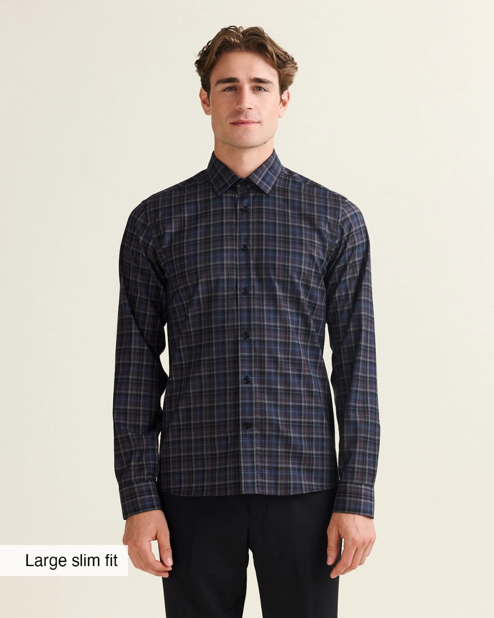 A man modeling a long-sleeve plaid Wolk merino shirt in a dark navy and black colorway, paired with black trousers, against a light beige background. A text overlay in the bottom-left corner reads 'Large slim fit'.