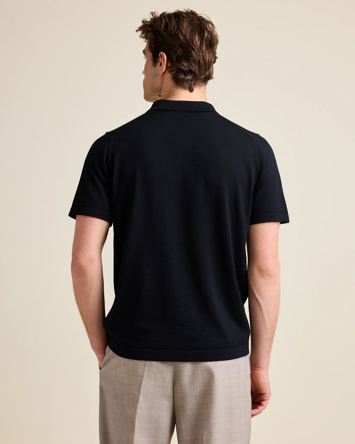 A male model in the studio wears a black merino wool polo shirt from the European brand Wolk.