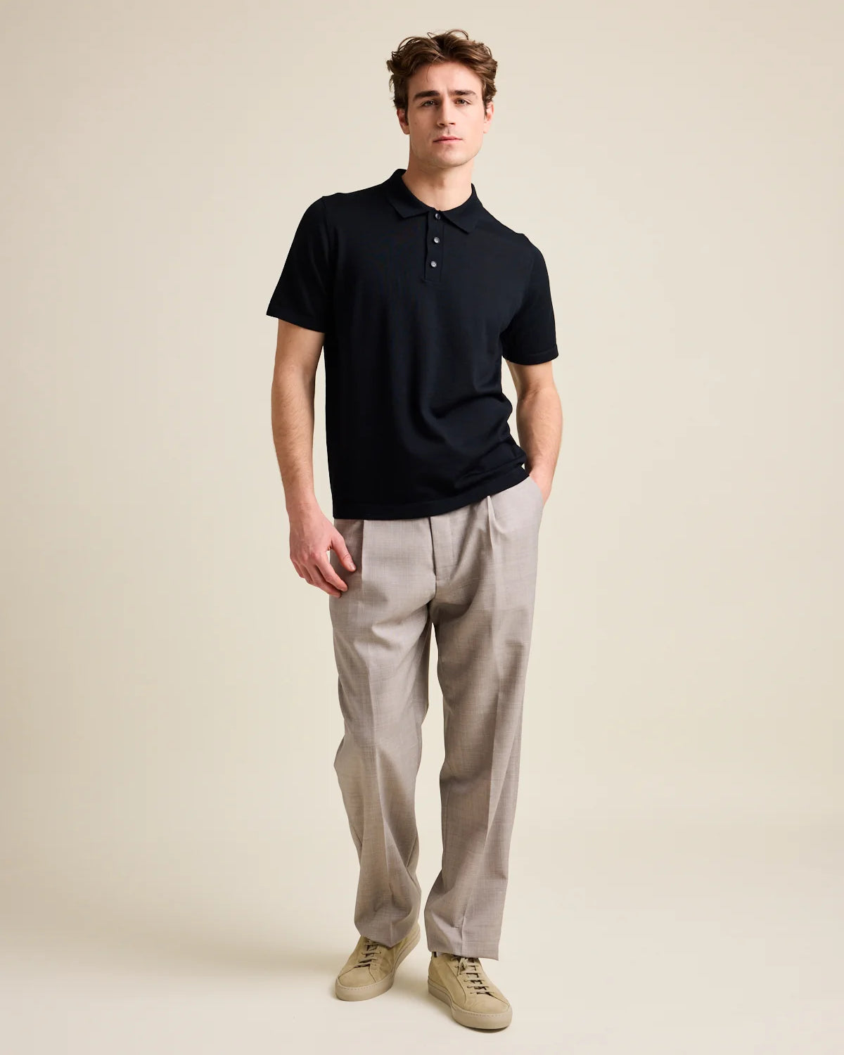 Model wears a black merino wool polo shirt with short sleeves.
