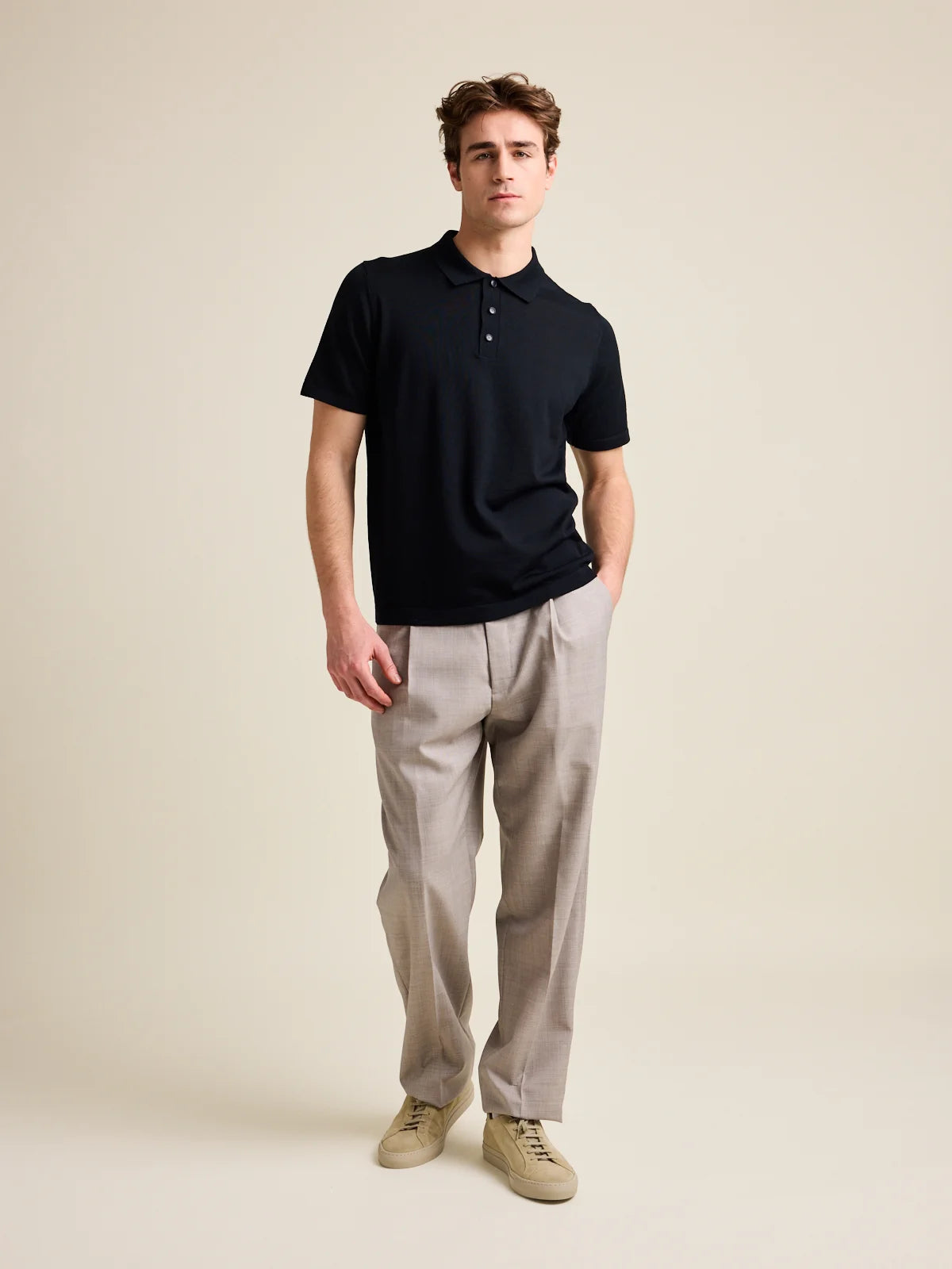 Model wears a black merino wool polo shirt with short sleeves.