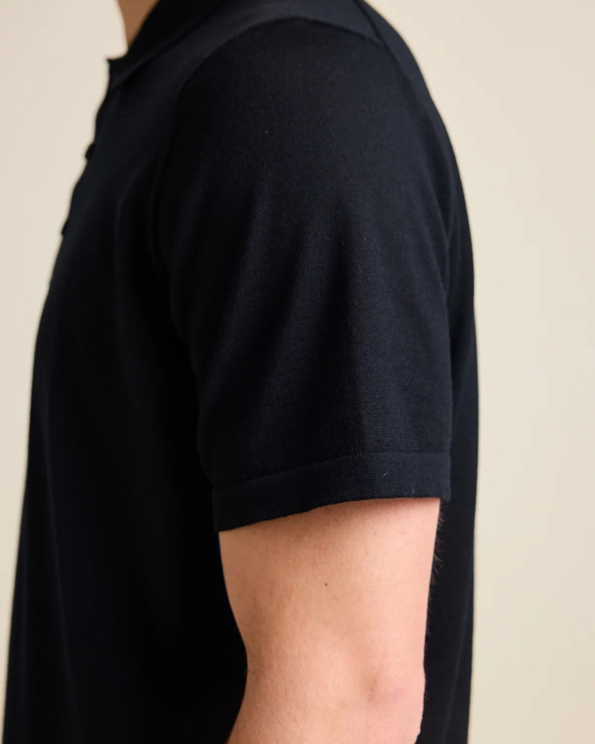 Close-up of the short sleeve on a men's black merino wool polo shirt by Wolk, showcasing the luxrious cashwool knit.
