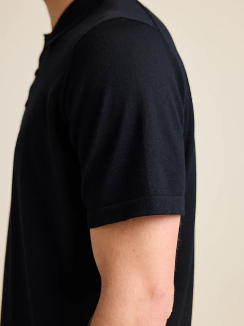 Gros plan sur les manches courtes d'un polo noir en laine mérinos pour homme signé Wolk, mettant en valeur la luxueuse maille de cashwool.