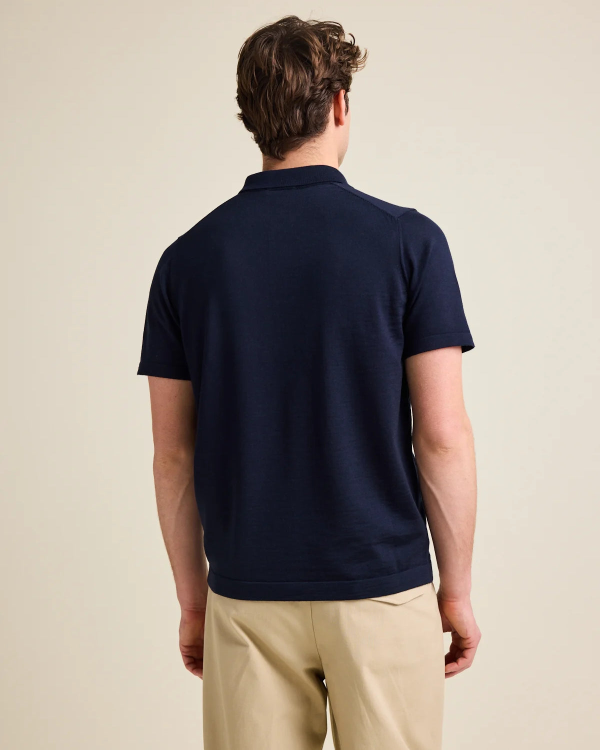 Back view of man wearing a short sleeve merino wool polo in dark navy blue color.