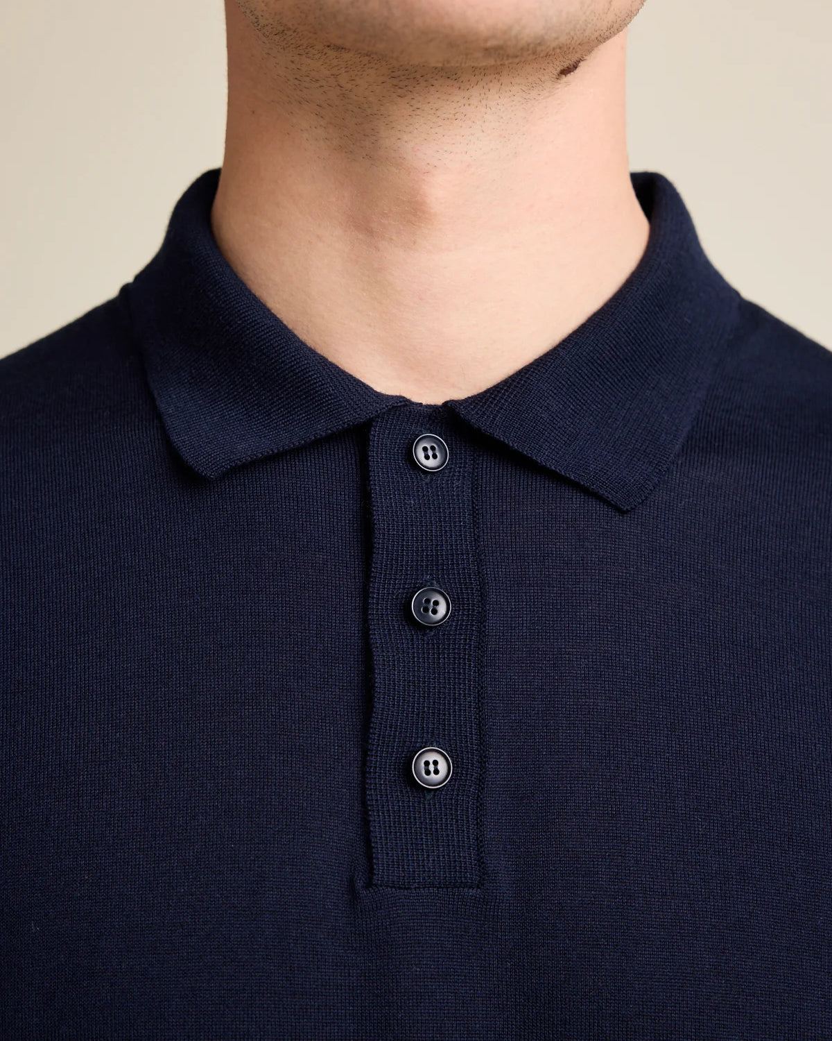 detail of knitted collar of a navy blue knitted merino wool polo shirt, with 3 corozo buttons in navy color.