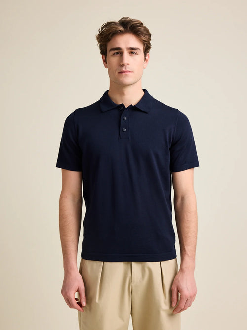 L'homme porte un polo en laine mérinos à manches courtes, tricoté avec de la laine mérinos extra fine zegna baruffa de couleur marine foncée de la marque européenne Wolk.