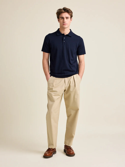 L'homme porte un polo en laine mérinos à manches courtes de Wolk, de couleur bleu foncé, avec 3 boutons et un col régulier.