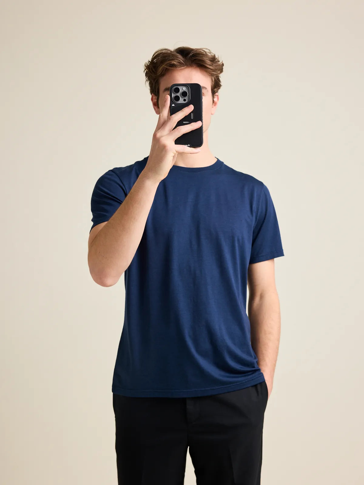 Man takes a picture of himself wearing a navy merino T-shirt from Wolk on black trousers