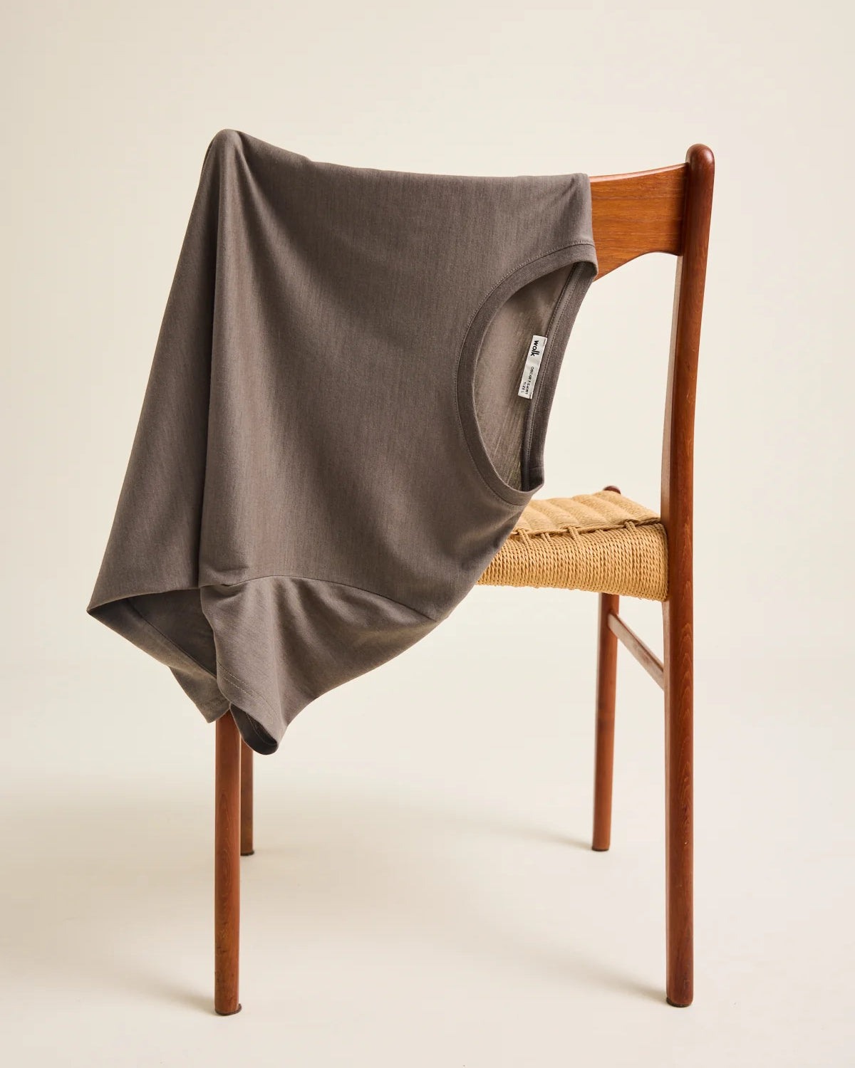A chocolate brown merino wool t-shirt from the brand Wolk is draped over a vintage chair in a studio setting.