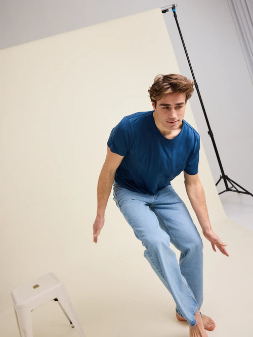 A male model in the studio wears a light medium blue colored merino wool crew-neck T-shirt from the European brand Wolk.
