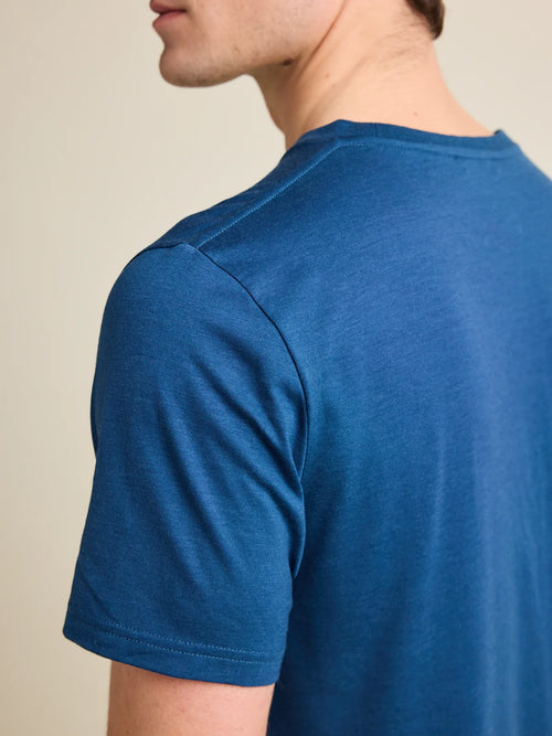 European-crafted, medium blue colored merino wool T-shirt for men by Wolk, focusing on the shoulder detailing in a studio setting.
