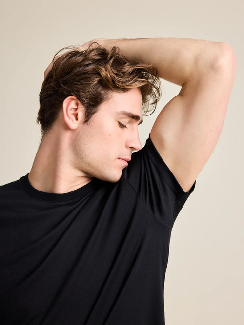 Man ruikt aan zijn oksel en draagt een geurvrij merino T-shirt in het zwart.