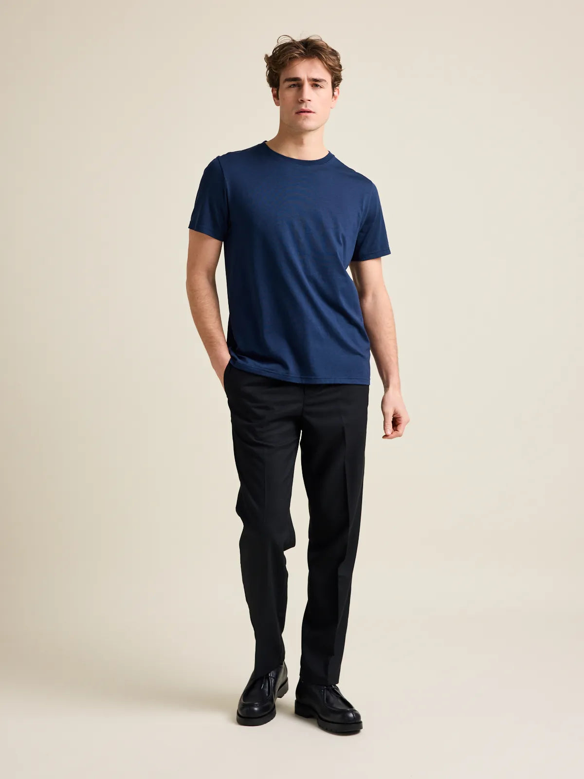 A male model in the studio wears a dark navy merino wool crew-neck T-shirt from the European brand Wolk.