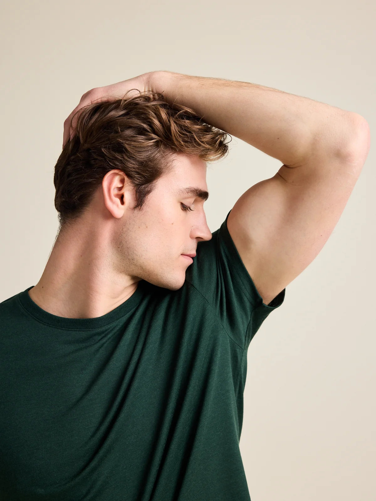 Men's dark green merino wool T-shirt from Wolk, model testing odour resistance and moisture control in a studio setting.