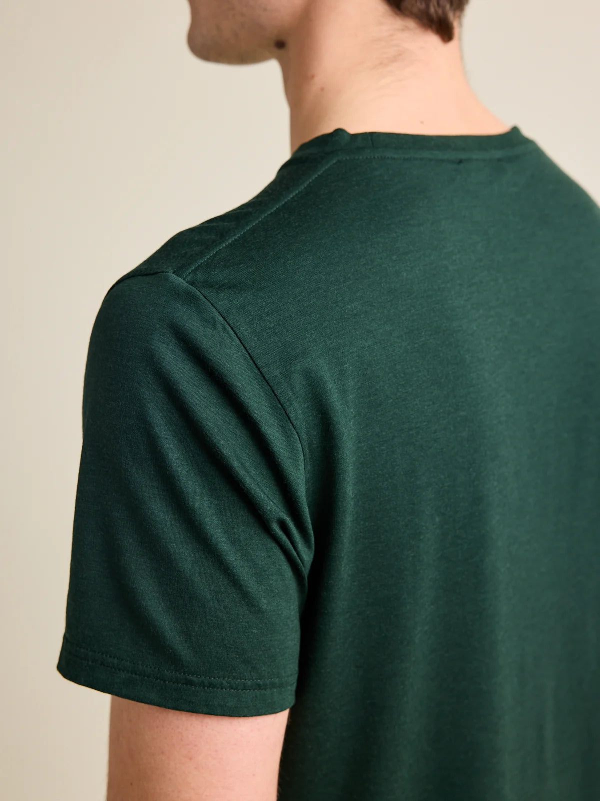 Close-up of the shoulder seam on a men's dark green merino wool T-shirt by Wolk, designed for durability and style.