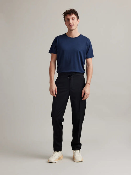 A male model in the studio wears a dark navy merino wool crew-neck T-shirt from the European brand Wolk.