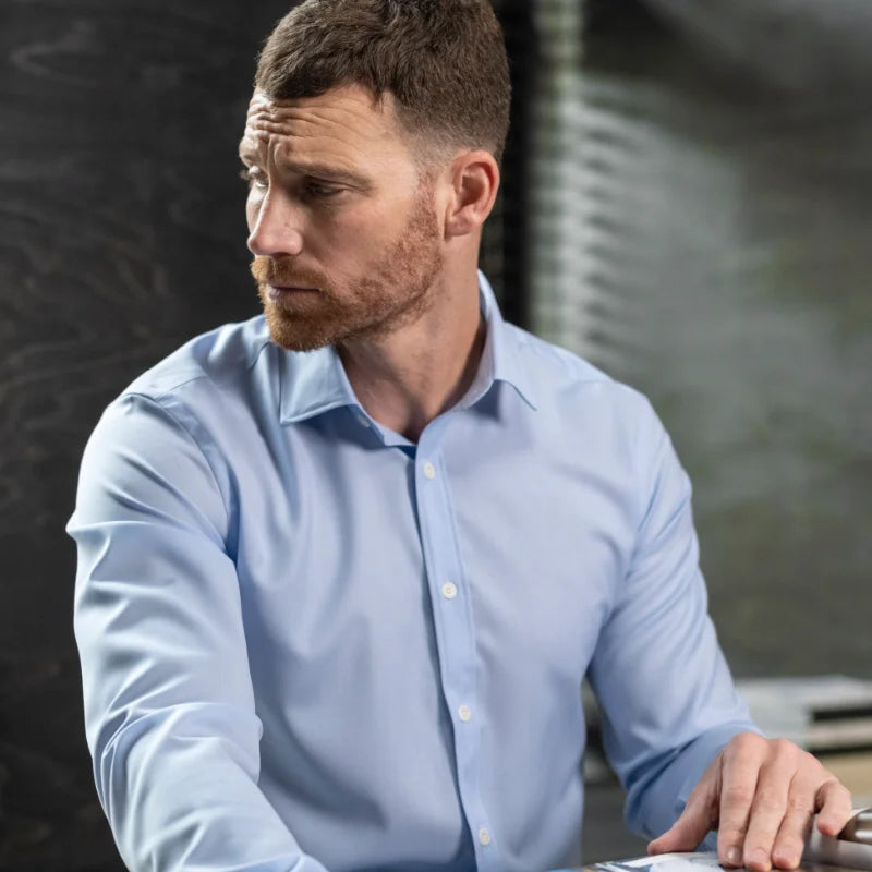 Man in a light blue merino shirt sitting at a desk with a blurred background