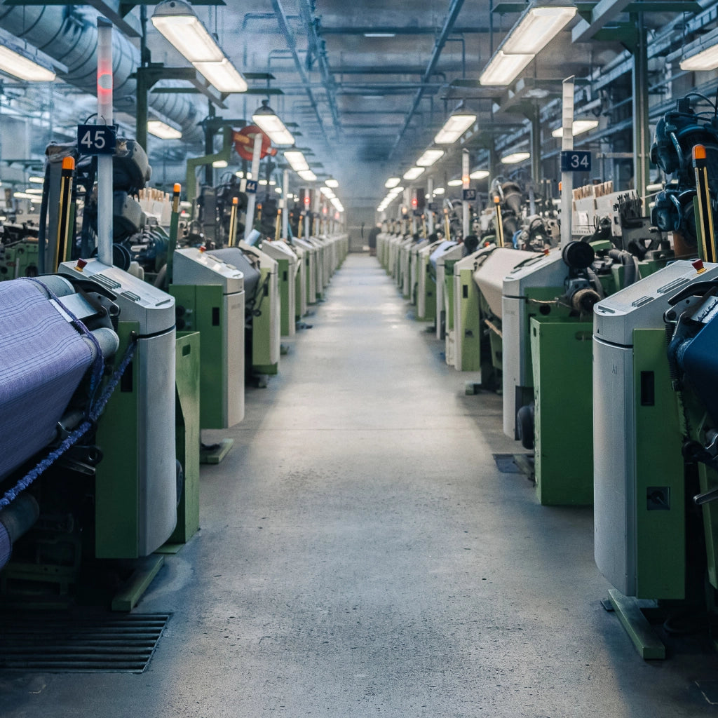 Factory interior with rows of automated weaving machines on a concrete floor.