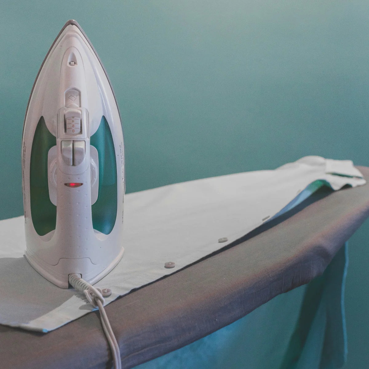 White iron on a gray ironing board against a teal wall