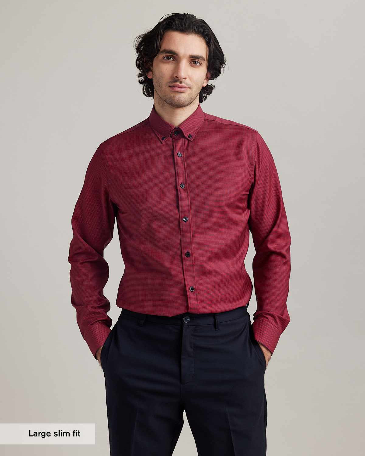 Man wears merino wool shirt with button down collar in red navy mini gingham pattern tucked in a navy blue trousers