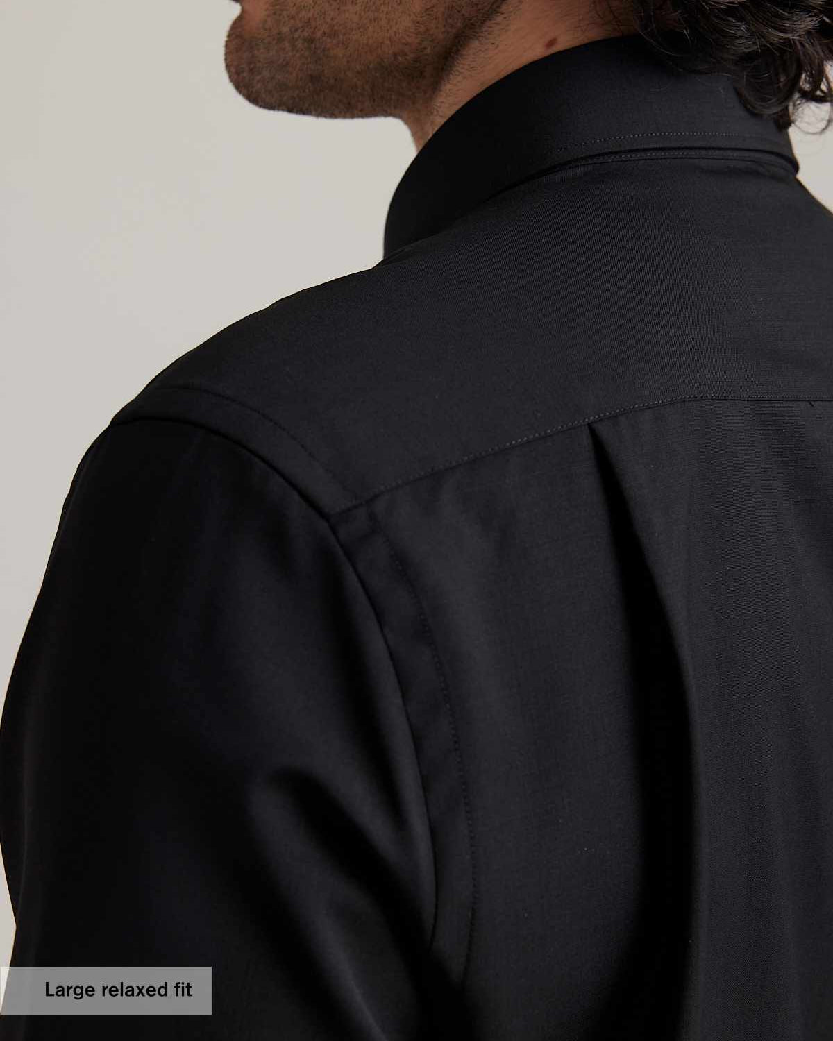 Close-up of a man wearing a black merino wool shirt. It shows the shoulder detail, the back pleat of the relaxed fit and the collar.