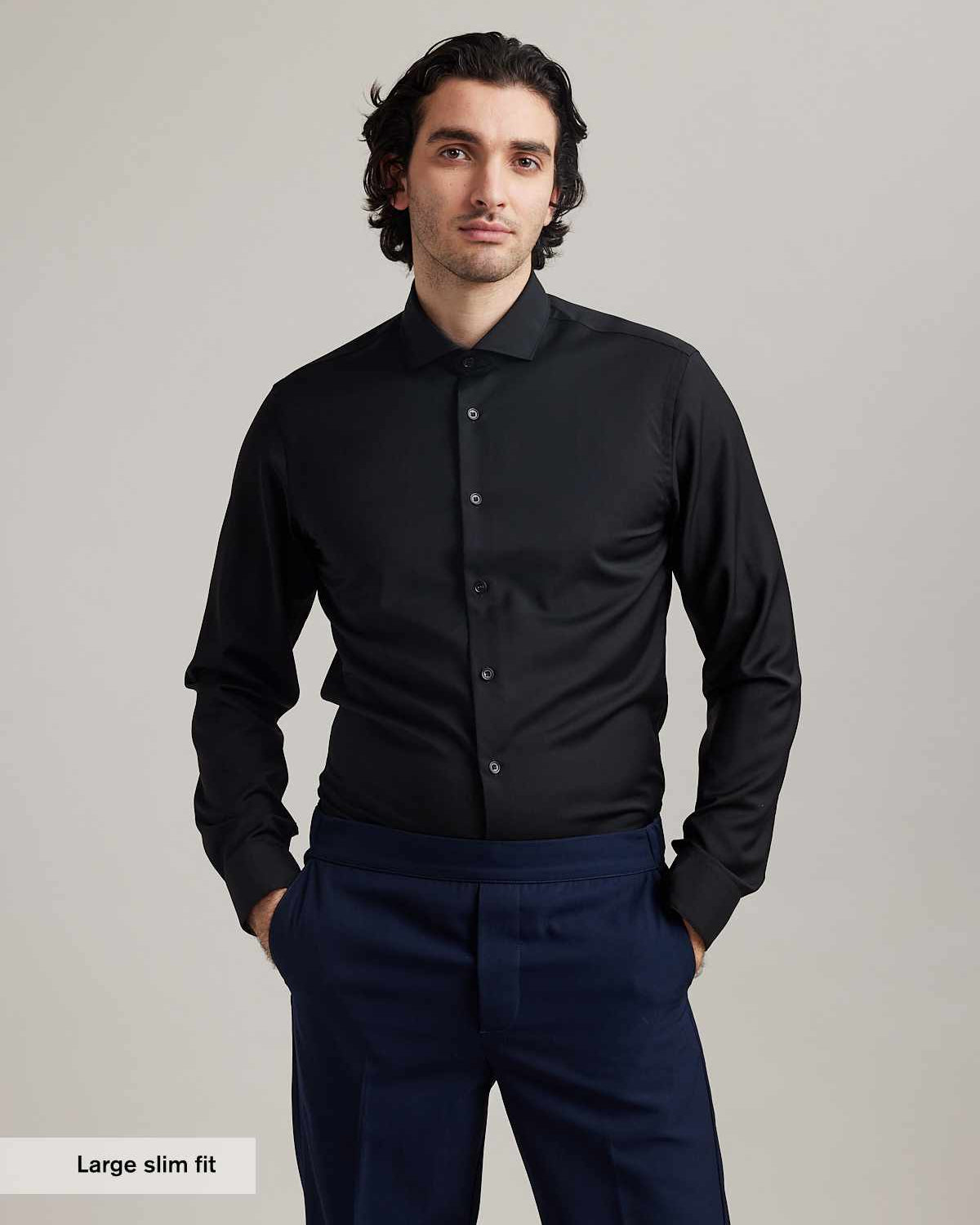 Man wearing a black merino wool shirt from Wolk and navy pants against a plain background