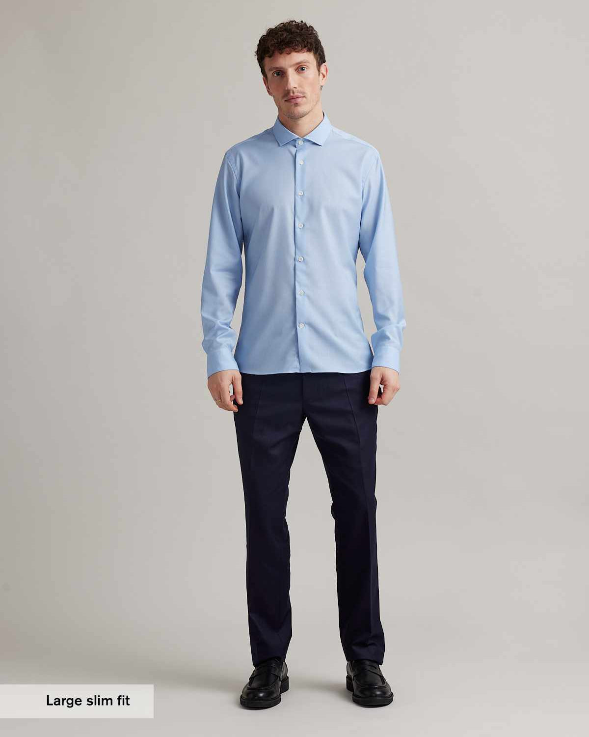 Man wears a light blue merino wool shirt with spread collar and white buttons in slim fit from Wolk