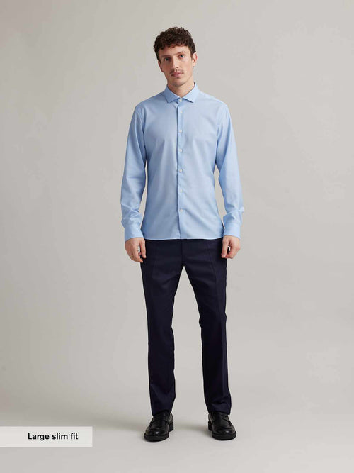 Man wears a light blue merino wool shirt with spread collar and white buttons in slim fit from Wolk