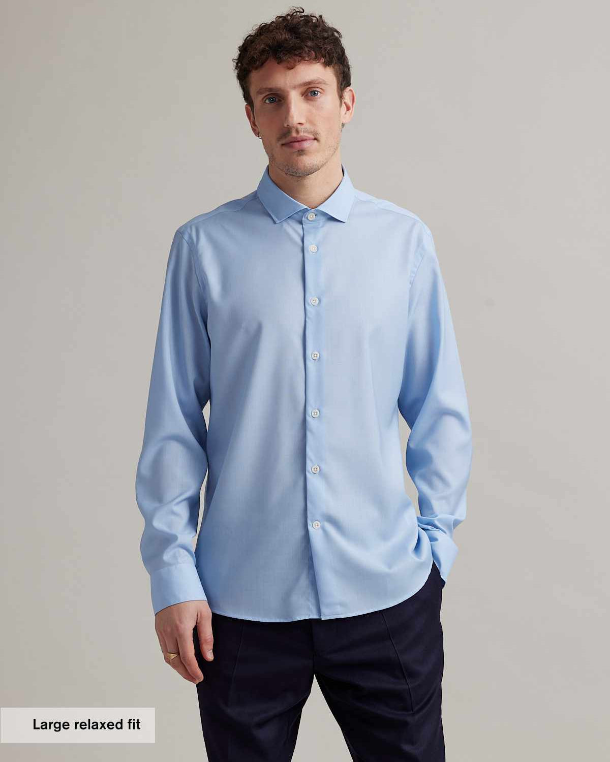 Man wears a light blue merino wool shirt with spread collar and white buttons in relaxed fit from Wolk
