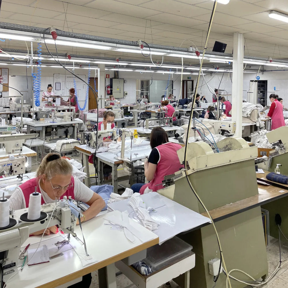 Factory floor with workers operating sewing machines in a busy production setting.