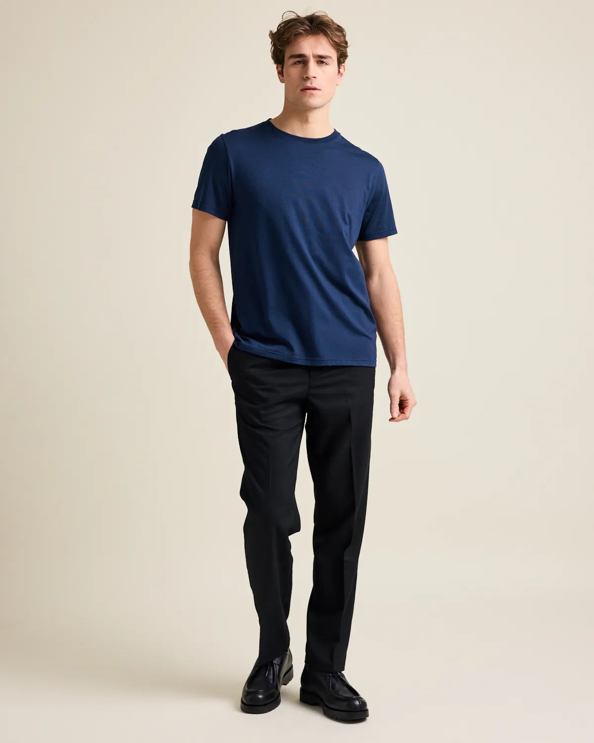 Man wearing a navy merinowool t-shirt and black pants on a beige background