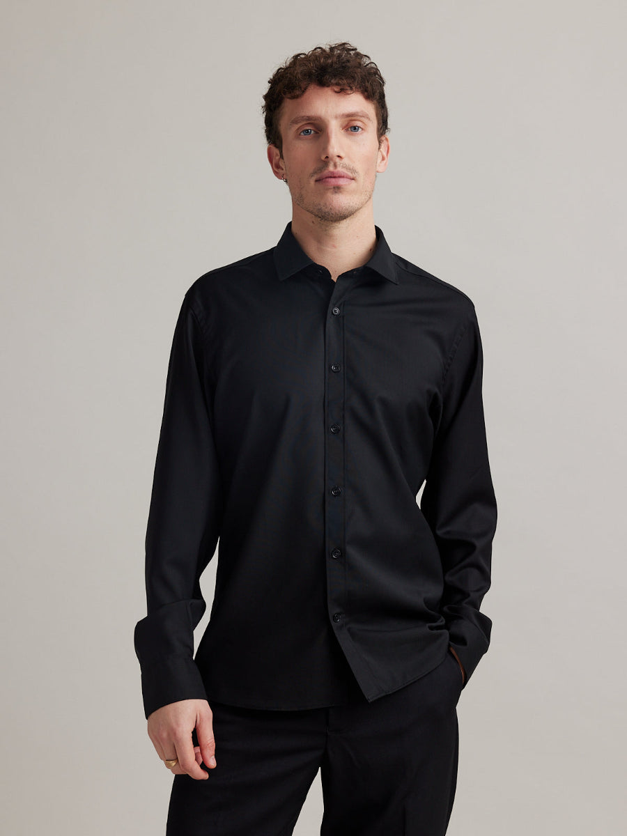 Man wears a black merino wool shirt with long sleeves, classic collar and black buttons in slim fit