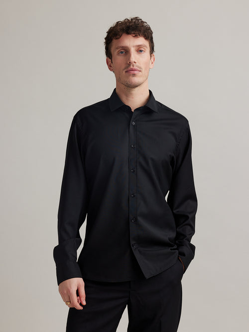 Man wears a black merino wool shirt with long sleeves, classic collar and black buttons in slim fit