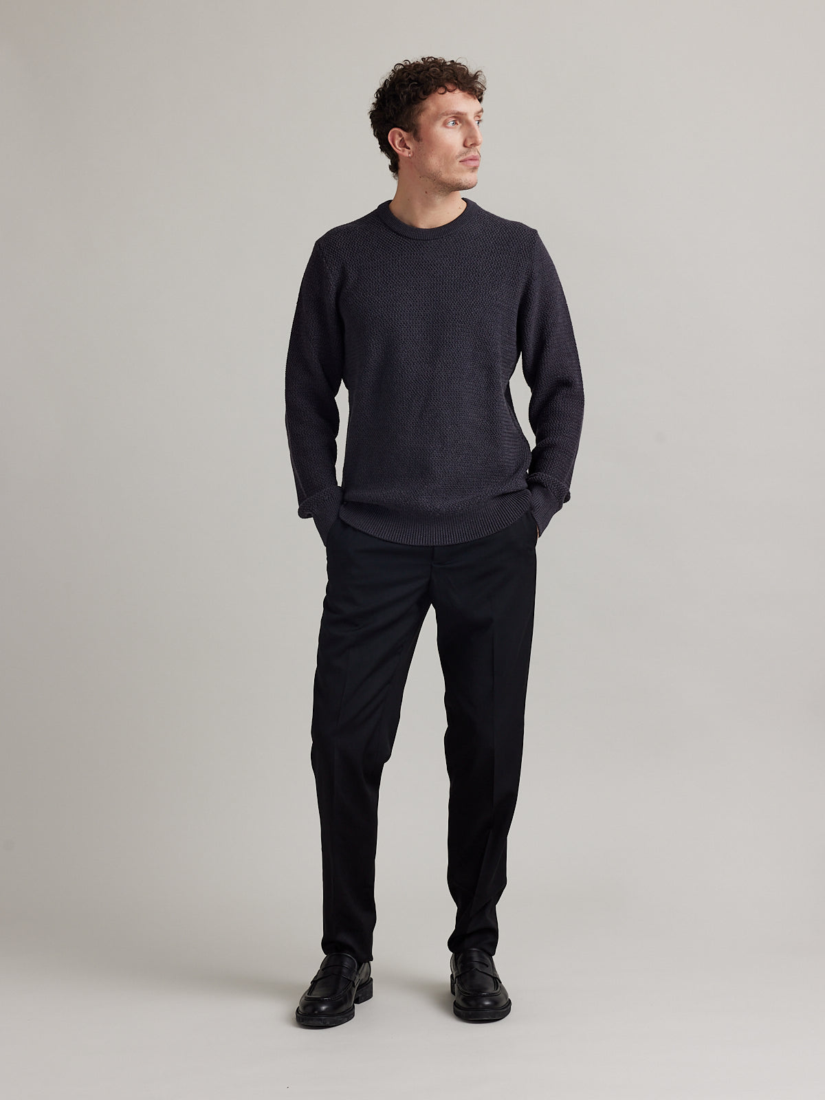 Man wears a dark grey merino wool sweater in rice knit with round collar and heavy weight warm jumper