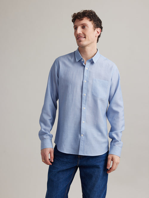 Man wears light blue chambray shirt in merino wool linen with white buttons and chest pocket and long sleeves