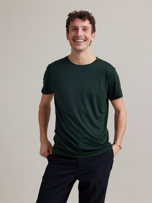 Man wears a short sleeve merino wool Tshirt in dark green with round neck in 170 g/sqm weight