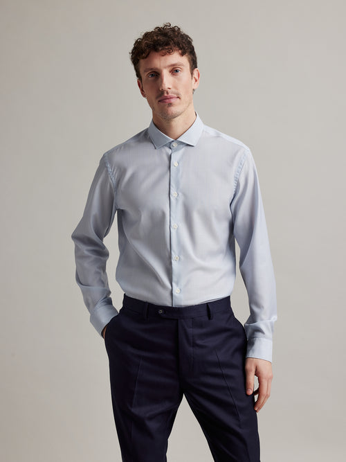 Man wears a light blue pinstripe merino wool formal shirt from Wolk with spread collar white buttons and long sleeves made in 100% merino wool