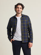 Man wears a merino flannel shirt in plaid blue green color with chestpocket open over a white merino wool T-shirt on a dark navy pants