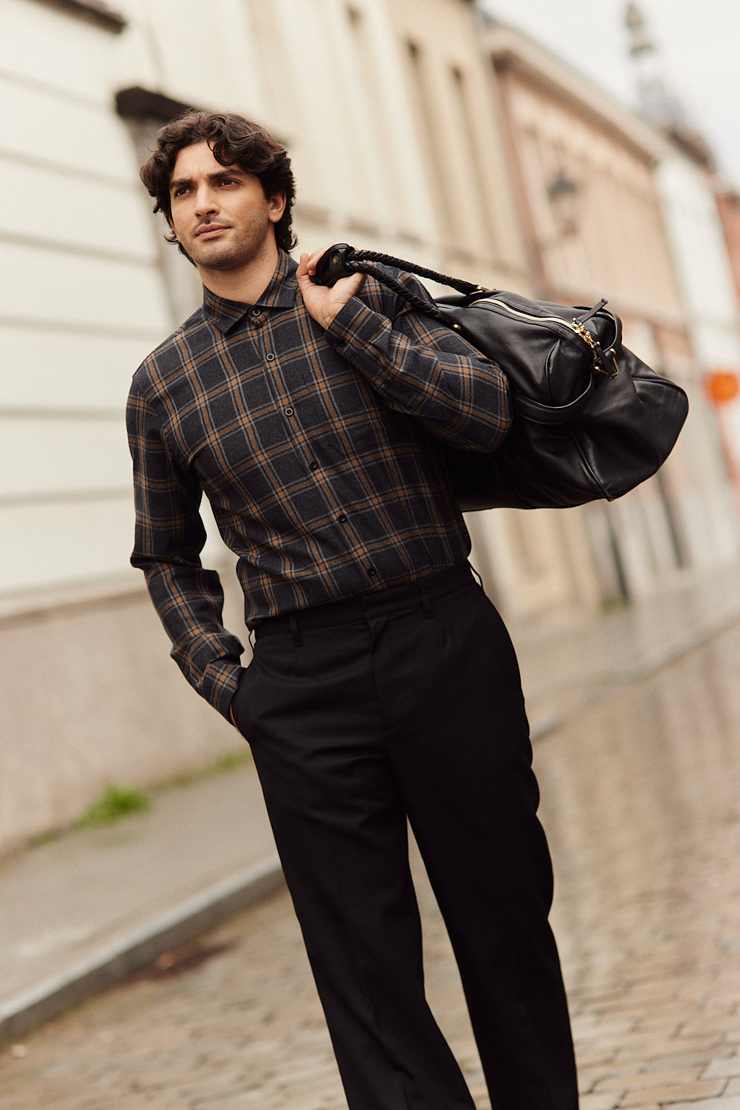 Man wears a merino wool flannel shirt  from Wolk in grey brown plaid pattern on a black trousers