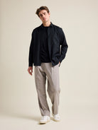 Man shows merino wool shirt from Wolk in black color on taupe wide fitted trousers.