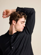 Man smells armpit. He wears a merino wool shirt from Wolk in black color which doesn't take up odours.