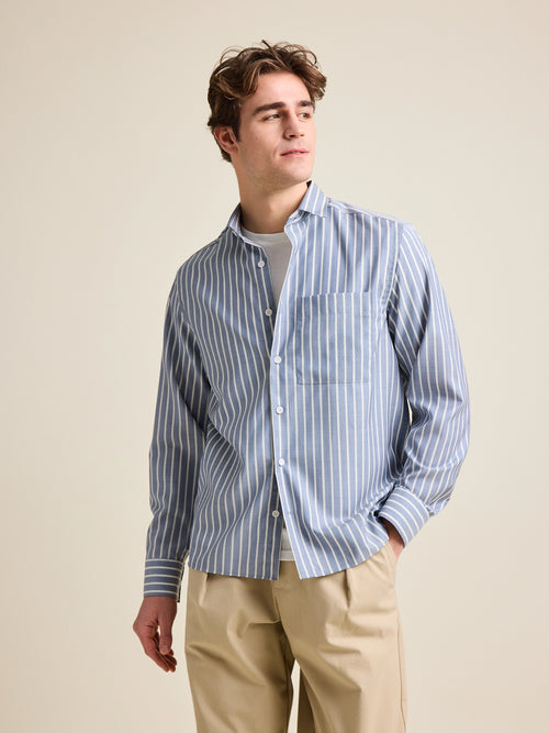 Man wears a merino wool shirt with long sleeves from Wolk. The merino shirt has a chest pocket and has a navy-white striped pattern. 