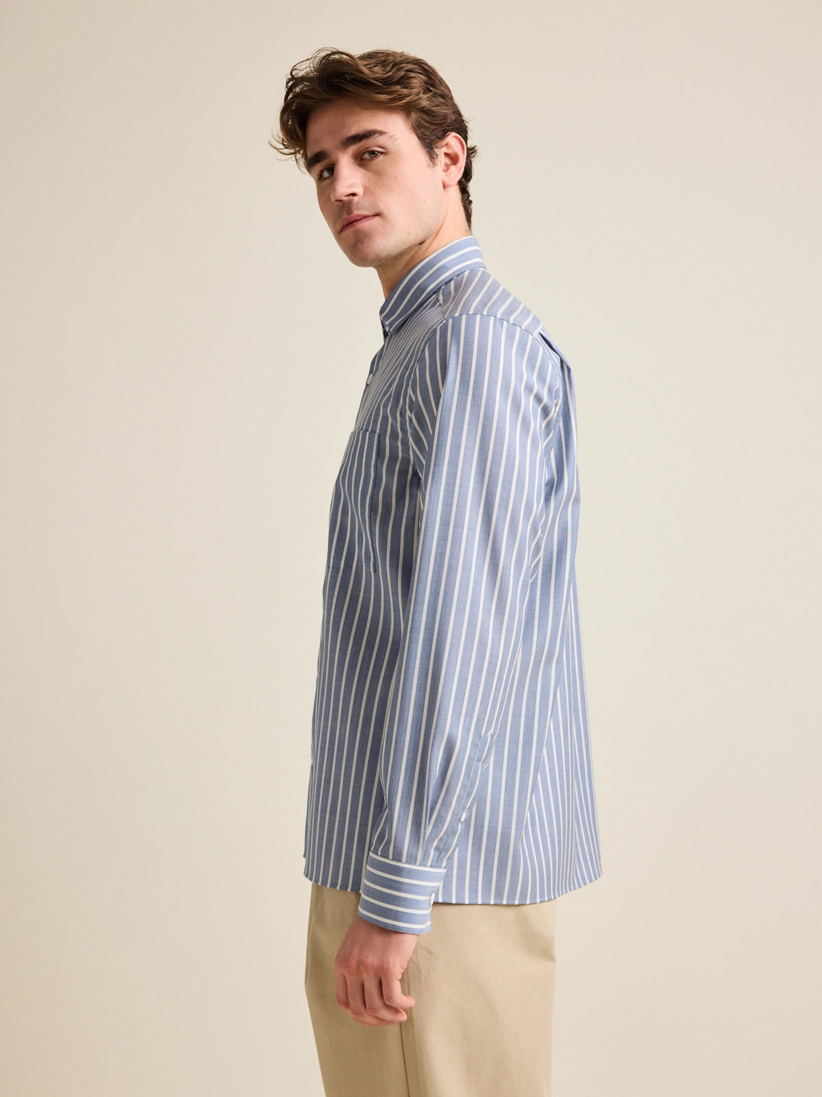 A side view of a man wearing a merino wool shirt with straight cut hem, in a relaxed fit with navy stripe pattern.