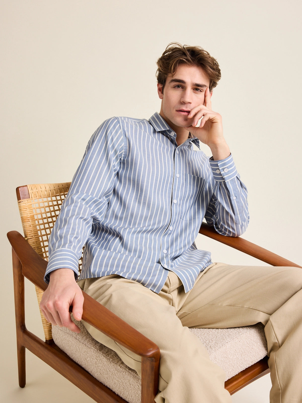 Man sits relaxed in a vintage chair. He wears a merino wool shirt from Wolk in a striped pattern with chest pocket.