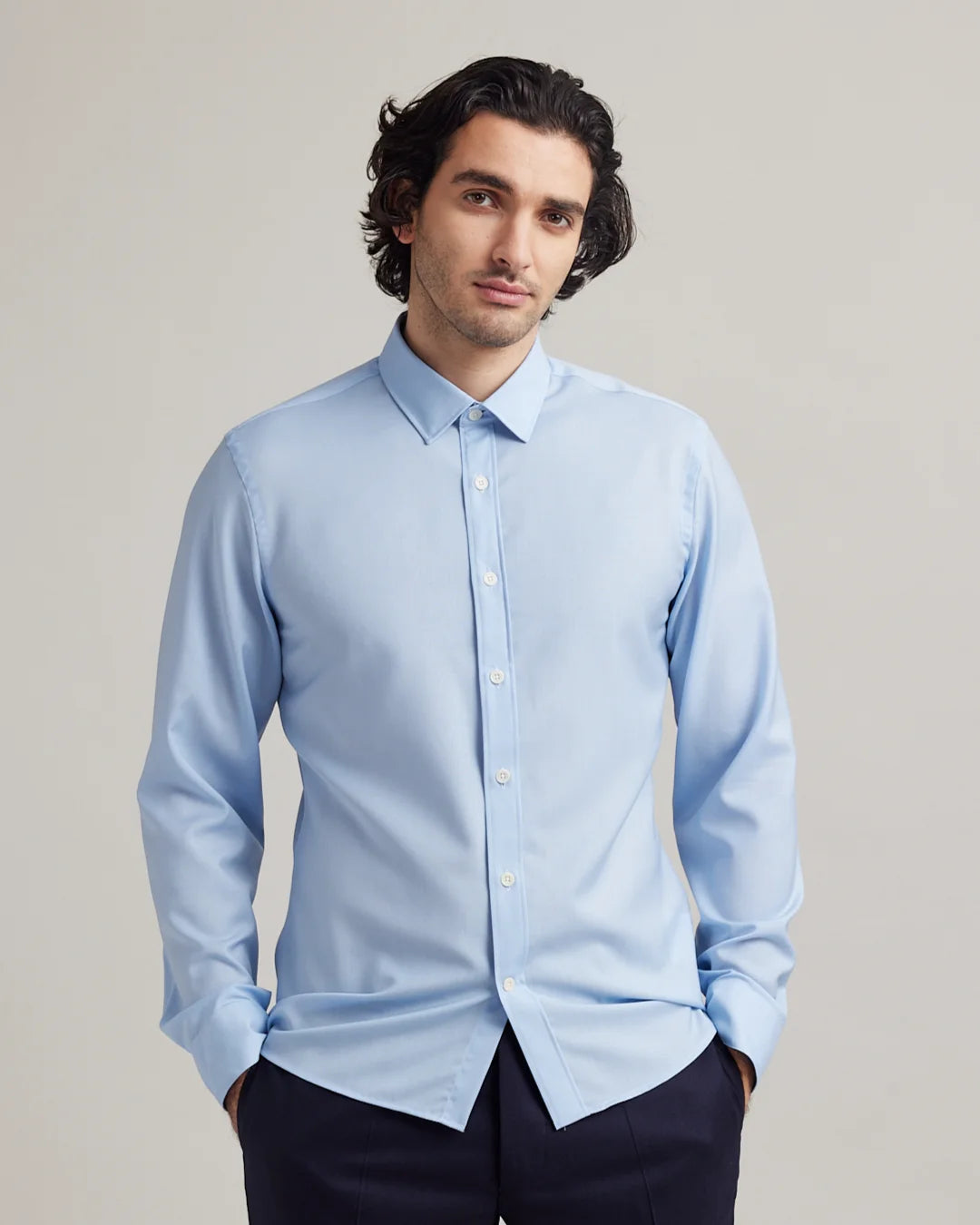 Man wearing a light blue dress shirt in merino wool against a plain background